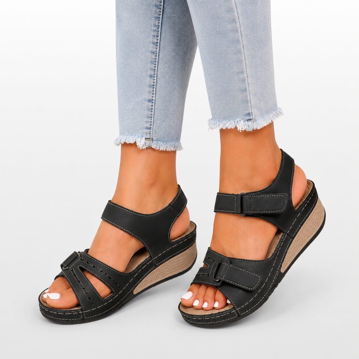 Black sandals worn with light blue jeans on a white background