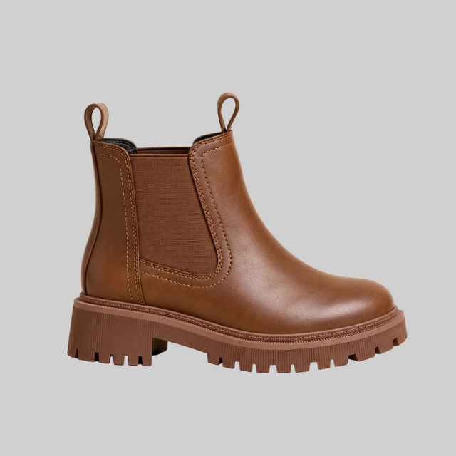 A single brown leather Chelsea-style ankle boot with elastic side gore panels, pull loops at the top, and a chunky lug sole, shown on a plain beige studio background.