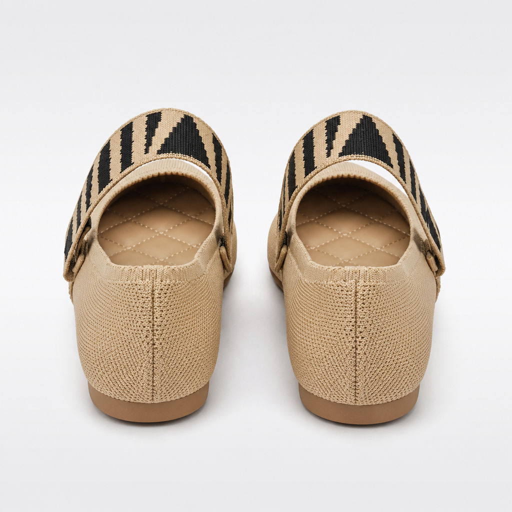 Pair of beige flat shoes with black and brown striped straps on a white background