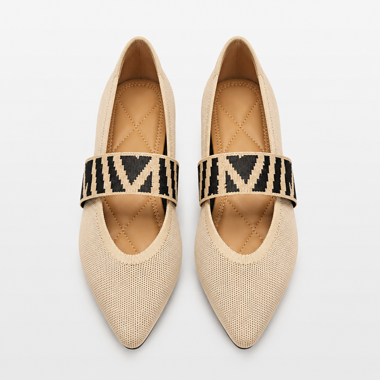 Pair of beige pointed-toe flats with black and white patterned straps on a light gray background