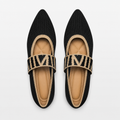 Pair of black pointed-toe flats with beige straps on a white background