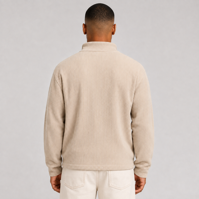 A man viewed from the back wearing a beige ribbed knit mock neck sweater and off-white trousers, set against a plain light gray studio background.