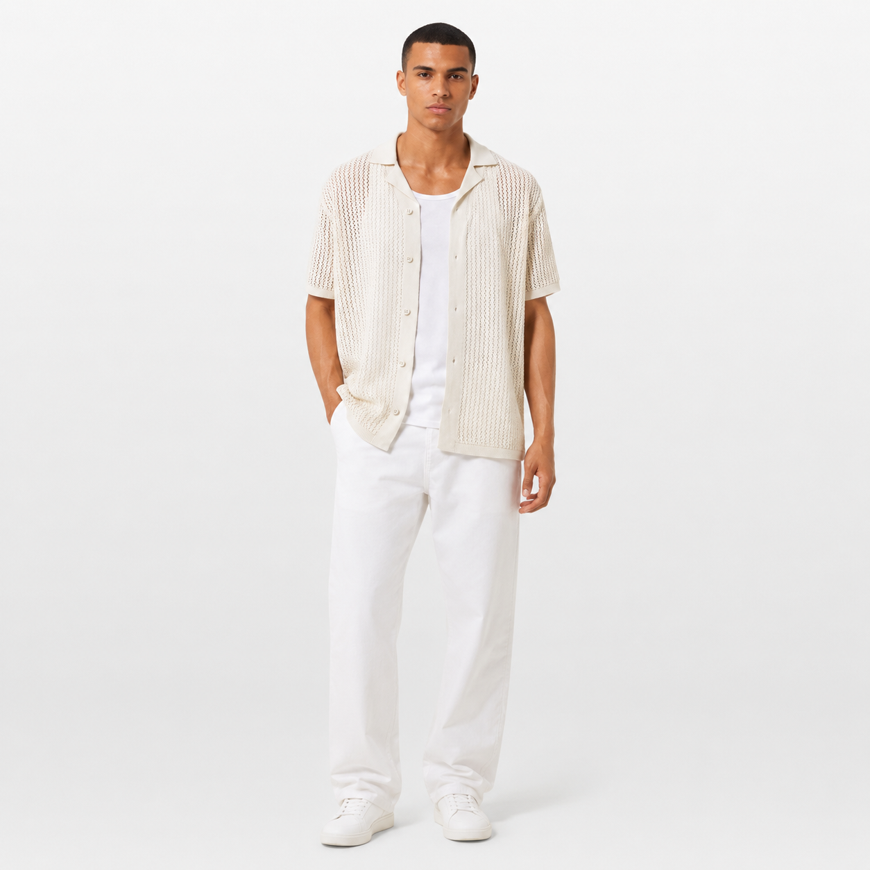 Man wearing a beige short-sleeve shirt over a white t-shirt with white pants on a white background