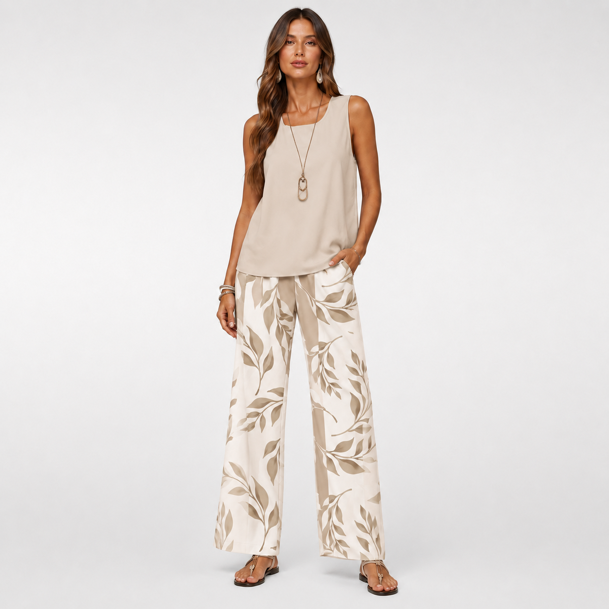 Woman wearing a beige sleeveless top and leaf-patterned pants on a white background