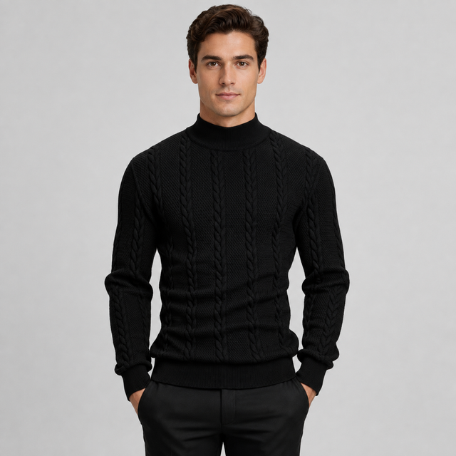 A man wearing a black cable-knit mock neck sweater and black trousers, standing against a light gray studio background.