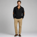 A man modeling a black knit polo sweater with tan elbow patches and a tan inner placket, paired with khaki pants and brown shoes, against a light gray studio background.