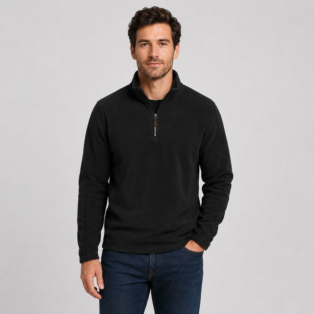 A man wearing a black long-sleeve quarter-zip pullover sweater and dark blue jeans, standing against a solid light gray background.
