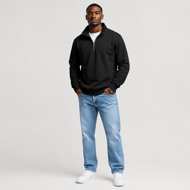 A man modeling a black quarter-zip sweatshirt, light-wash blue jeans, and white sneakers against a light gray studio background.