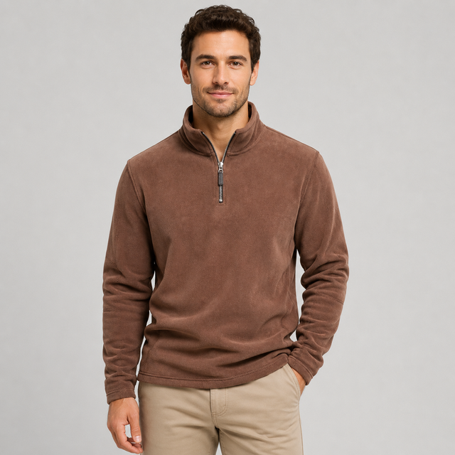 A man wearing a brown quarter-zip fleece pullover sweater and beige trousers, standing against a solid light gray background.
