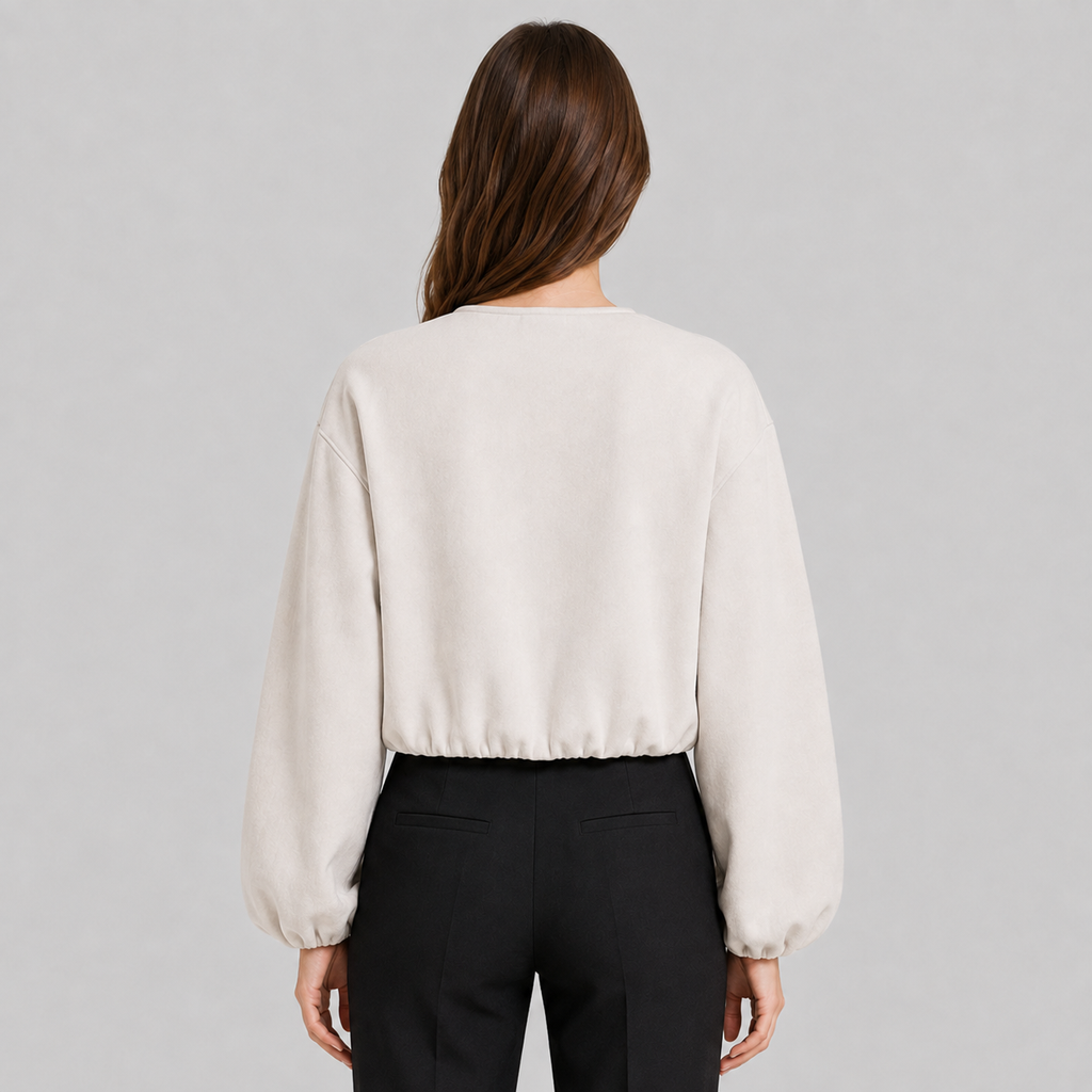 A woman viewed from the back wearing a cream-colored long-sleeve cropped sweatshirt and black pants, set against a solid light gray studio background.