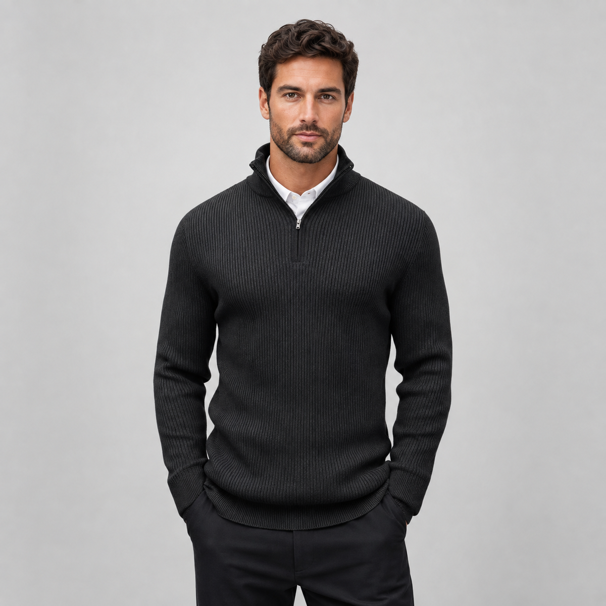 A man wearing a dark charcoal ribbed quarter-zip sweater over a white collared shirt, standing against a light gray studio background.