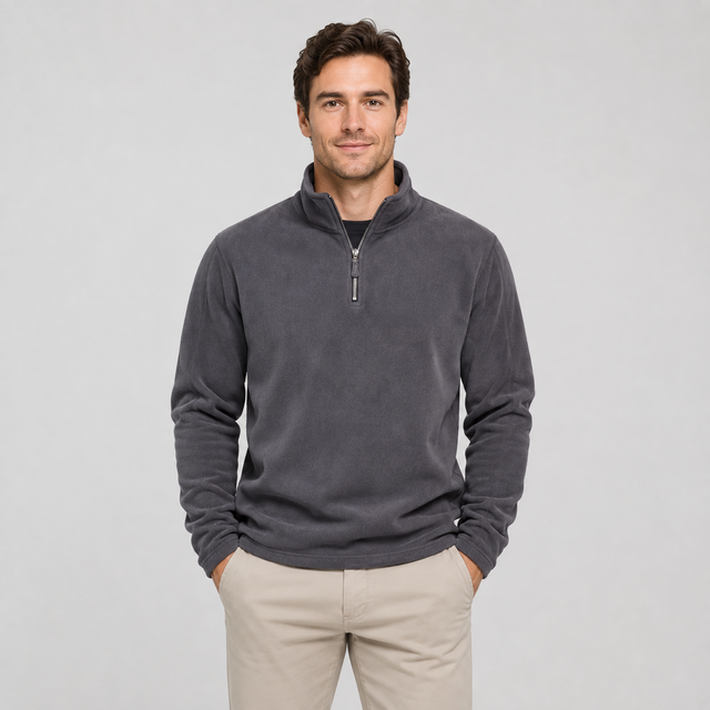 A man wearing a dark gray quarter-zip fleece pullover sweater and beige pants, standing against a light gray studio background.