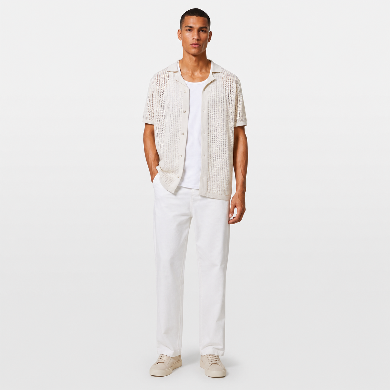 Man wearing a light-colored shirt and white pants on a plain background