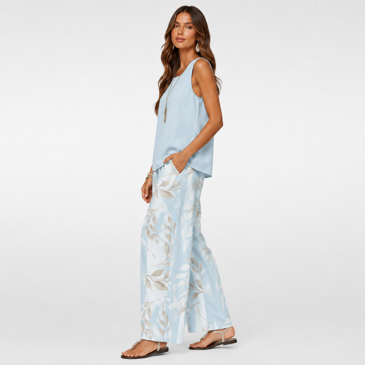 Woman wearing a light blue sleeveless top and floral pants on a white background