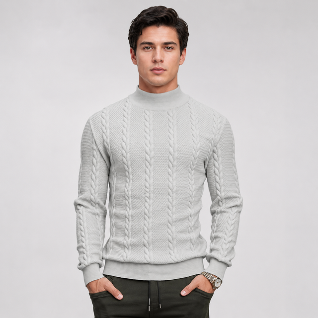 A man wearing a light gray cable-knit mock neck sweater, paired with dark pants, standing against a light gray studio background.