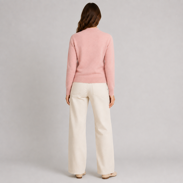 A woman shown from the back wearing a light pink knit sweater and off-white wide-leg trousers, standing against a neutral light gray studio background.