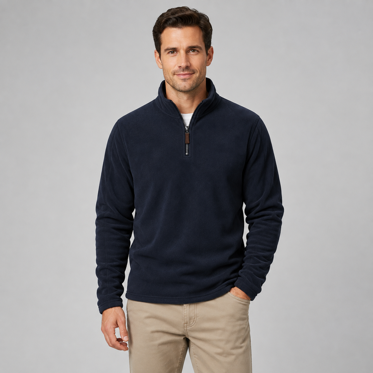 A man wearing a navy blue quarter-zip fleece pullover sweater and khaki pants, standing against a solid gray studio background.