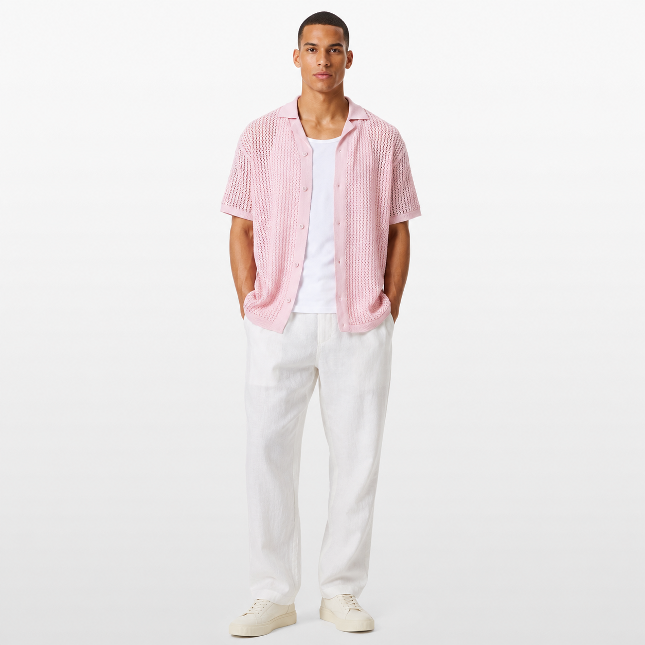 Man wearing a pink checkered shirt over a white t-shirt with white pants on a light gray background