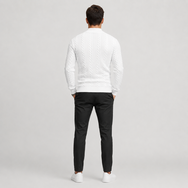 A man viewed from behind wearing a white cable-knit mock-neck sweater, black trousers, and white sneakers against a light gray studio background.