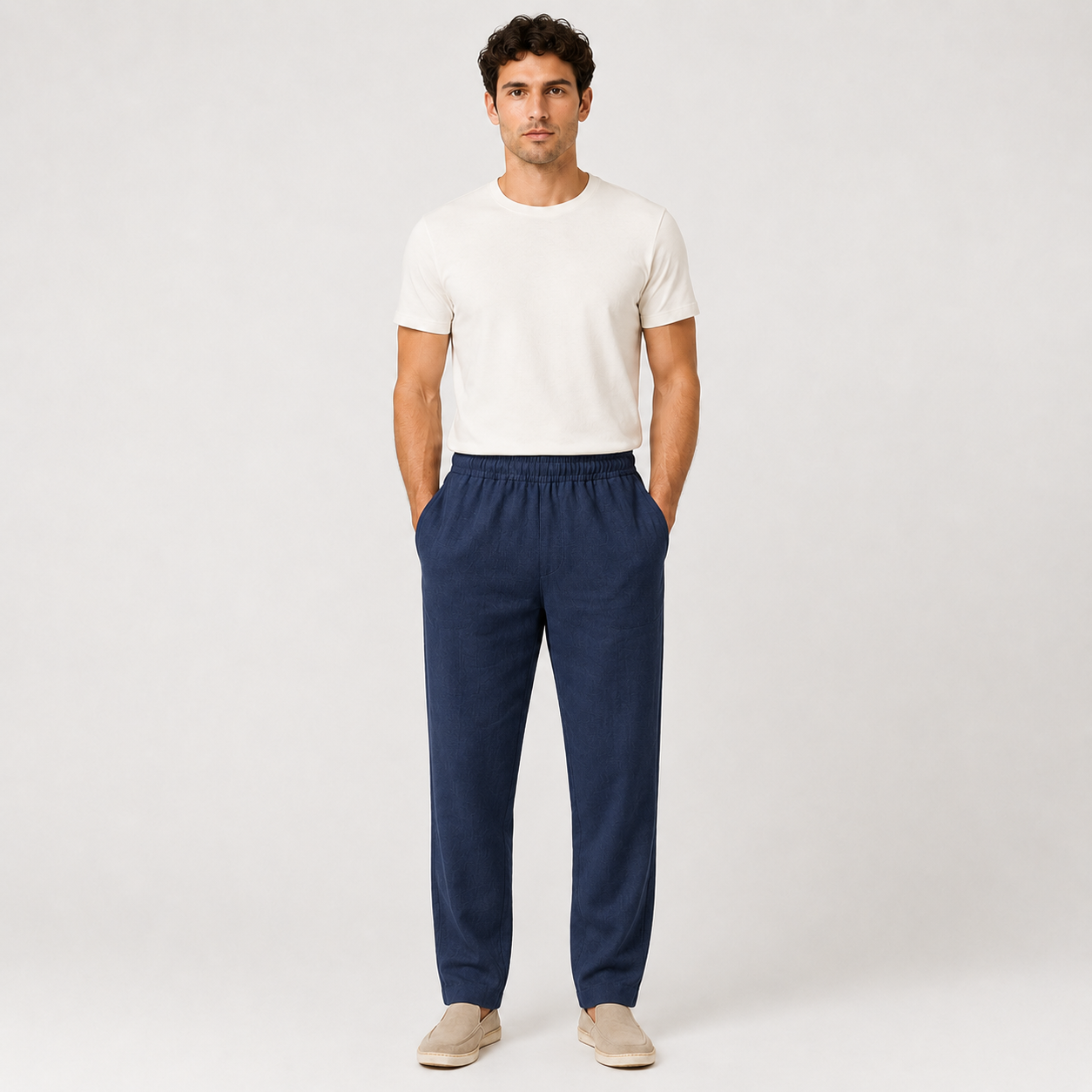 Man wearing a white t-shirt and navy pants on a plain background