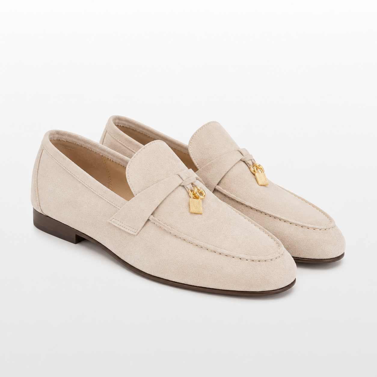 Pair of beige loafers with gold accents on a white background