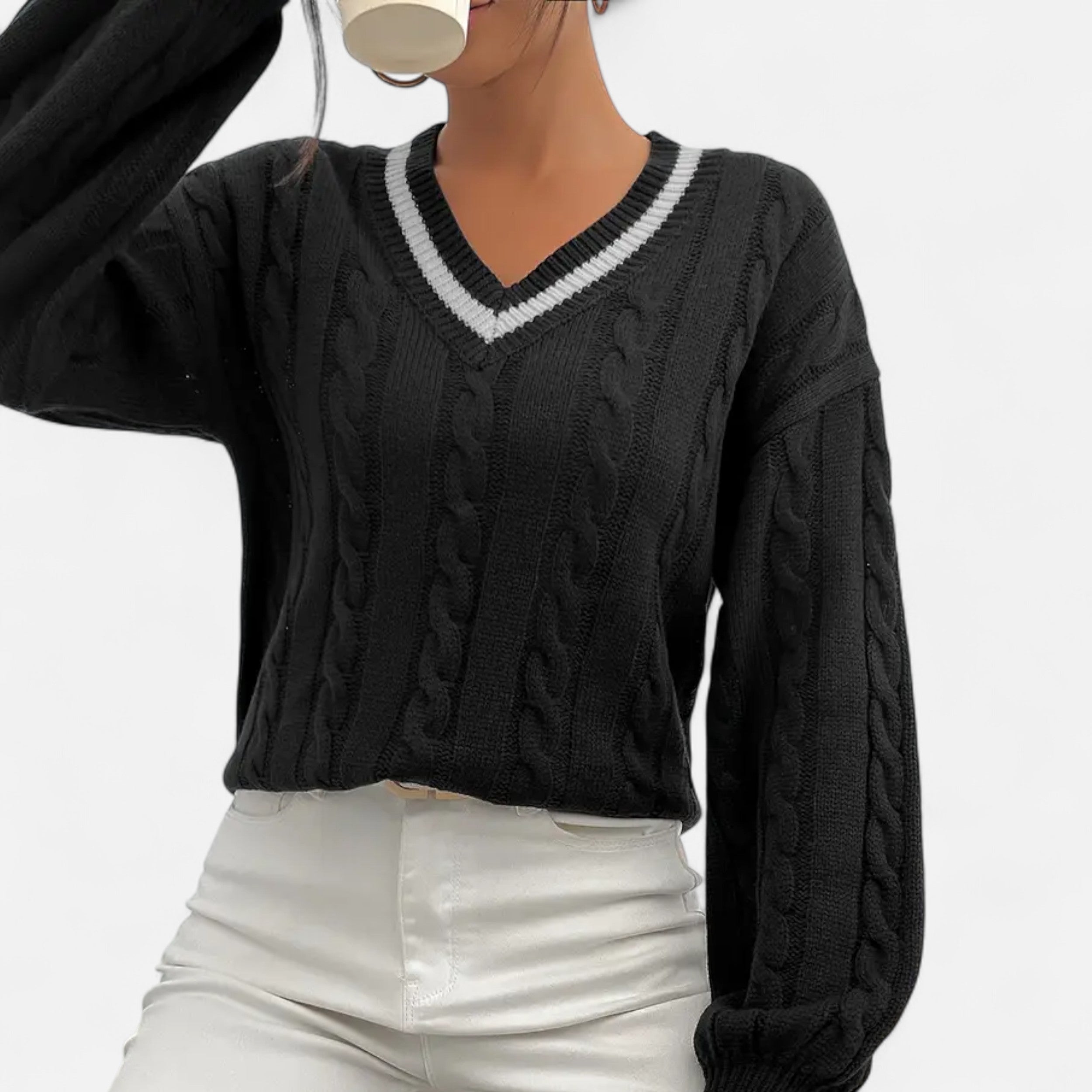 Person wearing a black cable knit sweater with white trim on a plain background
