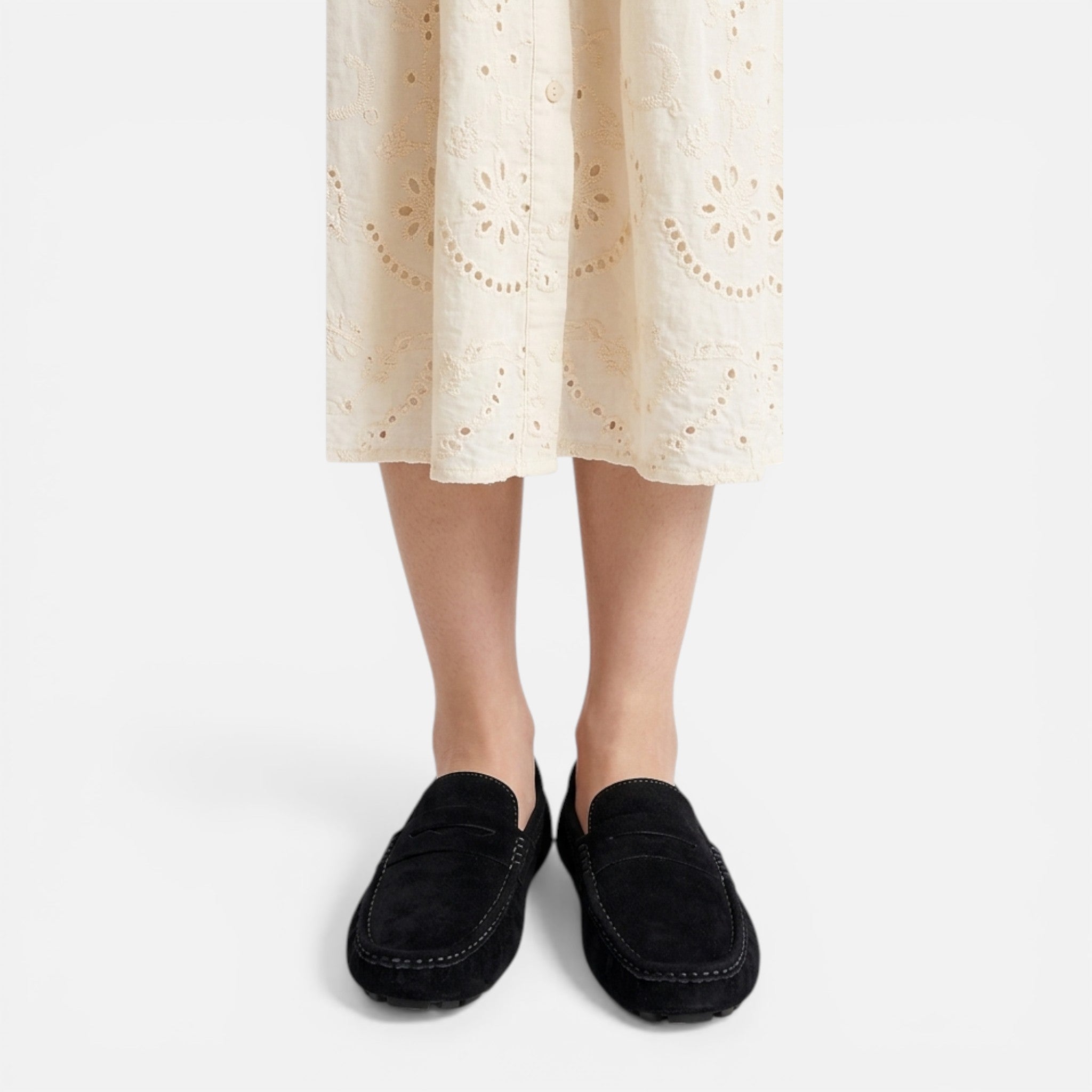 Person wearing black loafers and a beige lace dress on a white background