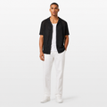 Man wearing a black textured shirt over a white shirt, paired with white pants on a white background