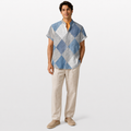 Man wearing a blue and gray checkered shirt with beige pants on a white background