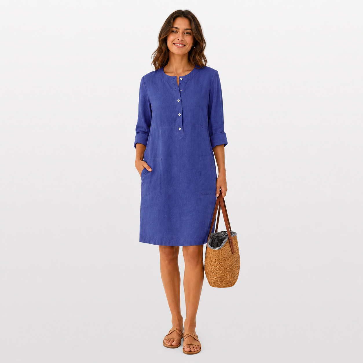 Woman wearing a blue dress holding a woven bag on a white background