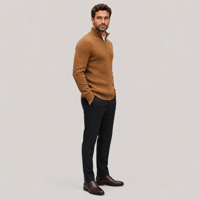 A man modeling a brown quarter-zip knit sweater, paired with dark trousers and brown leather shoes, standing against a solid light gray background.