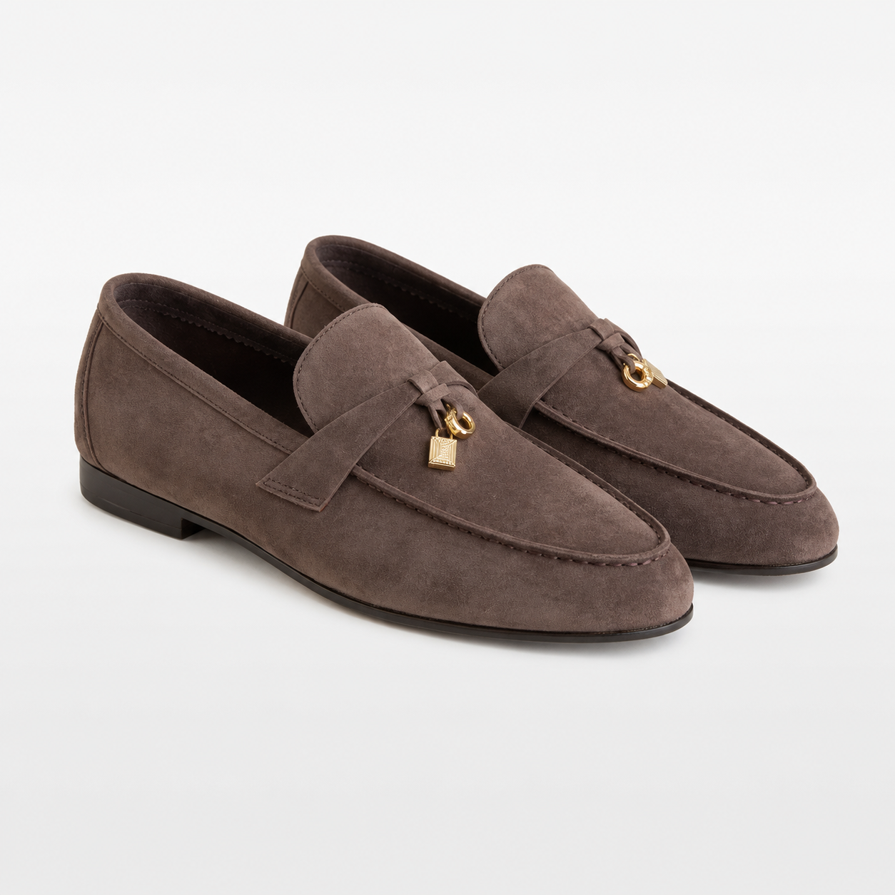 Pair of brown suede loafers with a gold tag on a white background