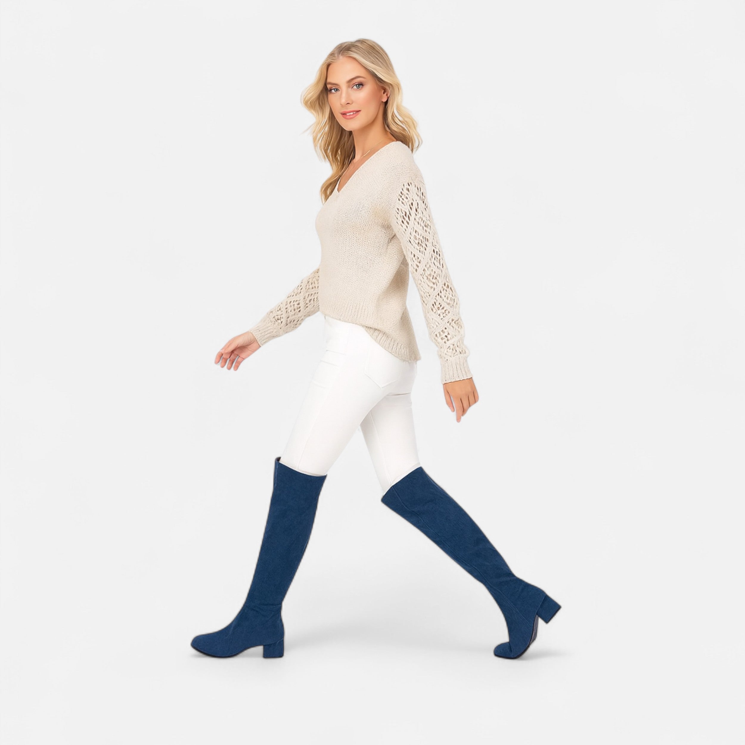 Woman wearing a cream sweater and white pants with blue knee-high boots on a white background