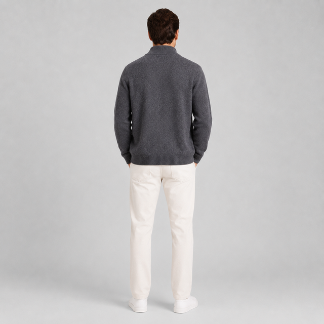 A man viewed from behind wearing a dark gray knit sweater and off-white trousers, standing against a light gray studio background.