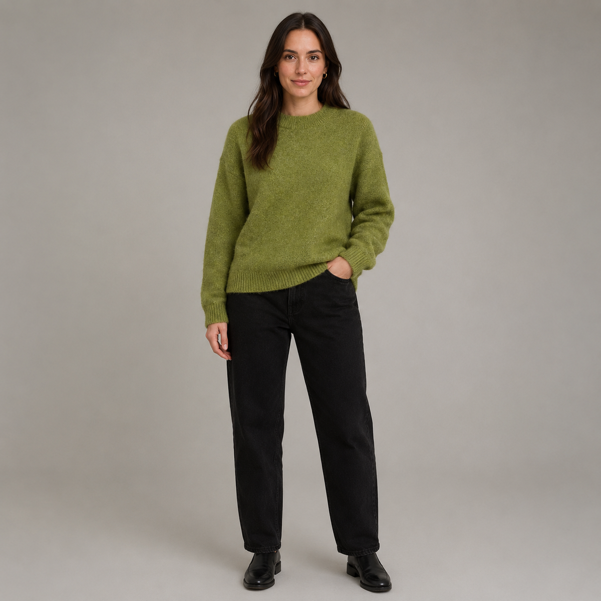 A woman modeling a fuzzy olive green crewneck sweater paired with black trousers and black shoes, standing against a neutral gray studio background.