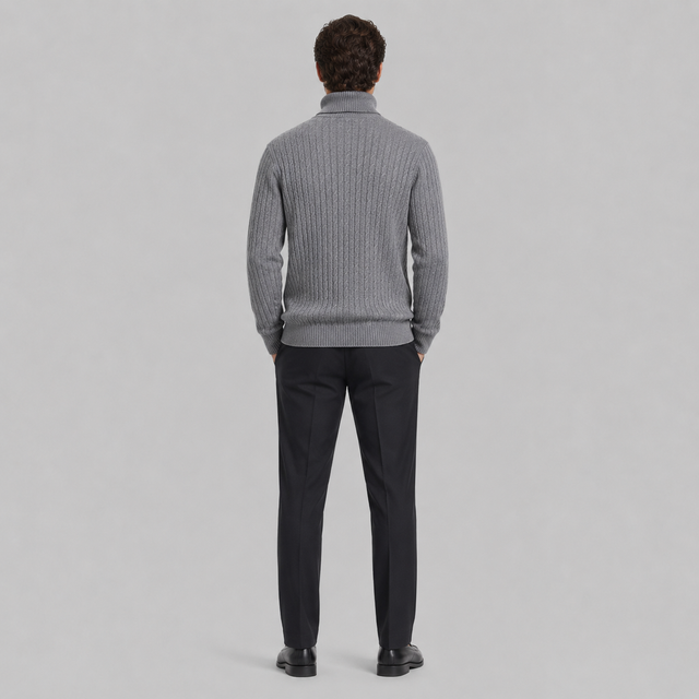 A man viewed from behind wearing a gray ribbed knit mock-neck sweater and dark trousers, standing against a light gray studio background.