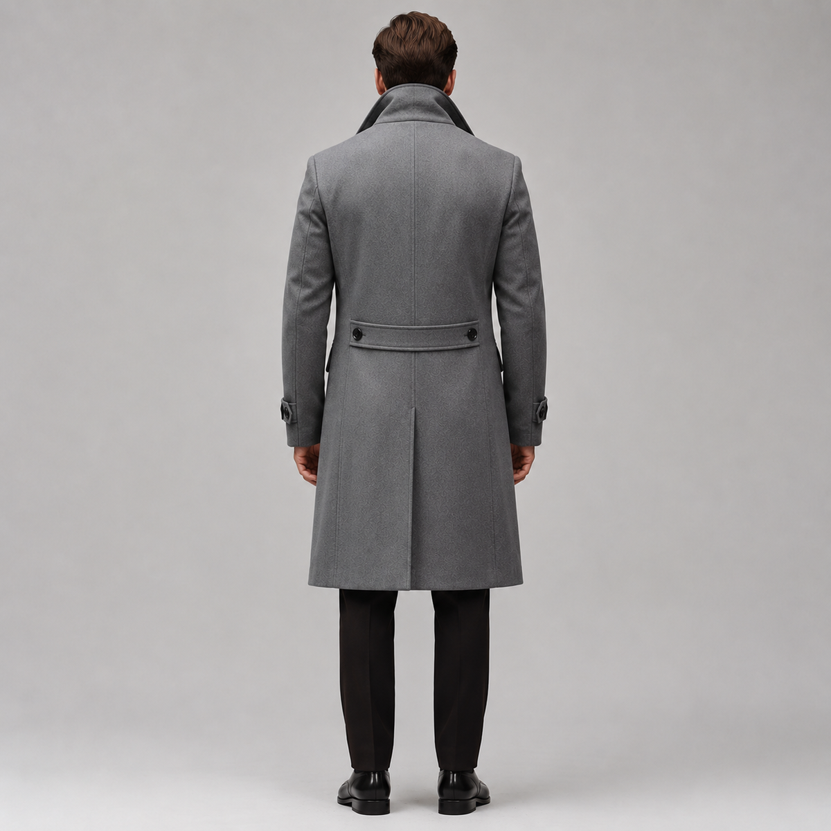 A man viewed from behind wearing a mid-length gray wool overcoat with a dark collar, black trousers, and black shoes, standing against a light gray studio background.