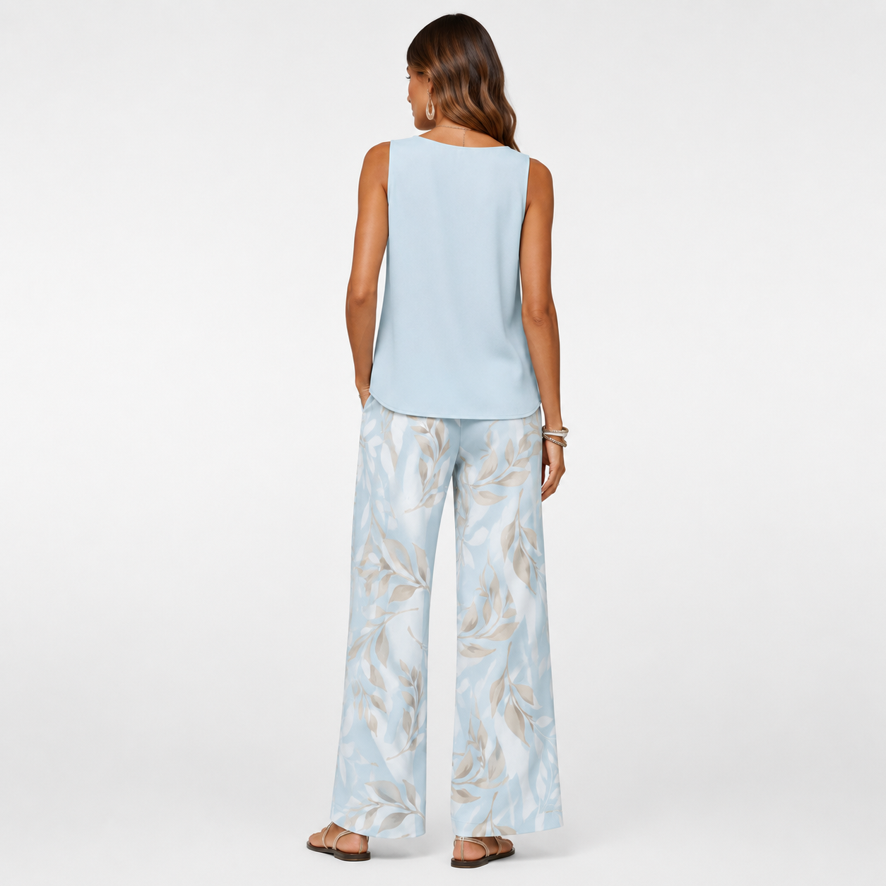 Woman wearing a light blue sleeveless top and patterned pants on a white background