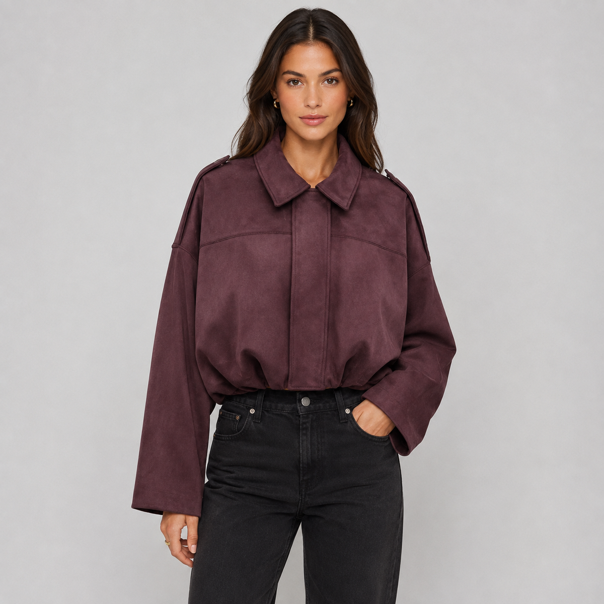 A woman modeling a cropped, long-sleeve collared jacket in a deep plum-burgundy color, paired with black jeans, against a solid light gray studio background.