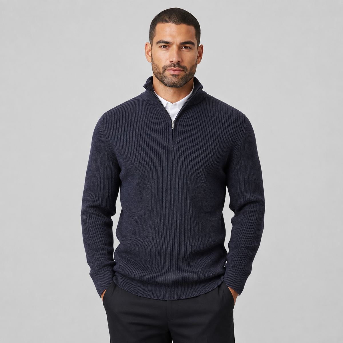 A man wearing a navy blue ribbed knit quarter-zip sweater over a white collared shirt, standing against a light gray studio background.