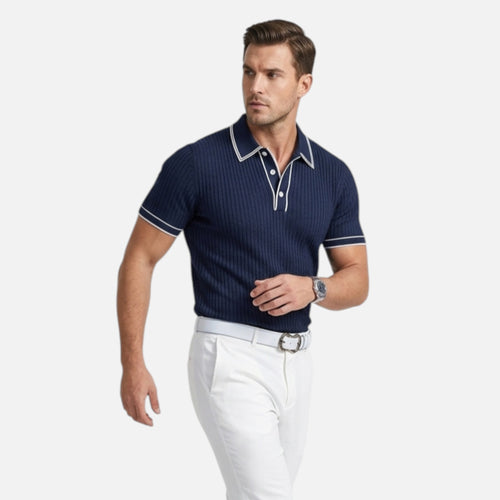 Man wearing a navy polo shirt with white trim and white pants on a light gray background