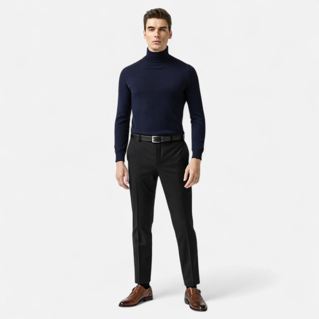 Man wearing a navy turtleneck and black pants on a white background