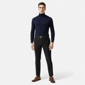 Man wearing a navy turtleneck and black pants on a white background