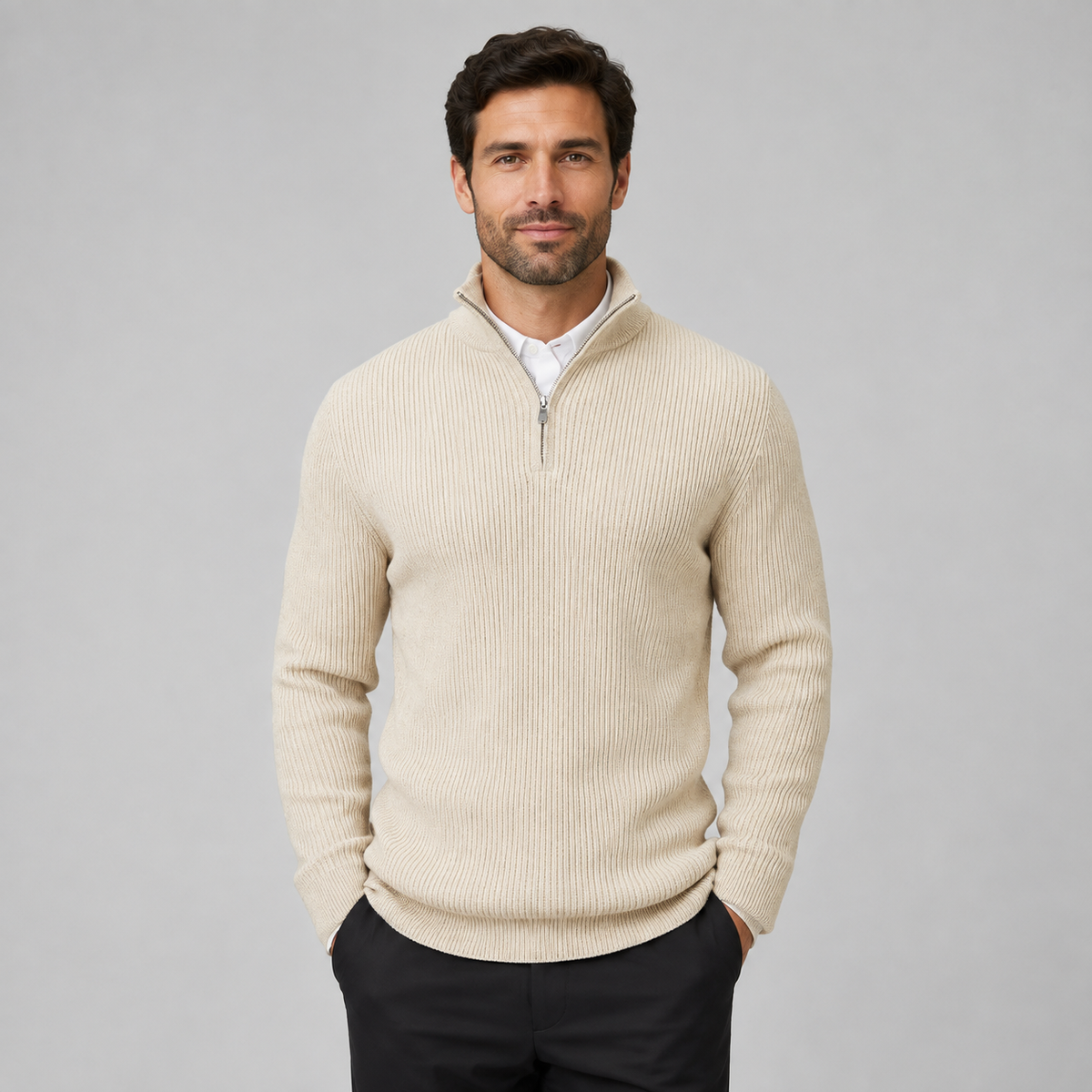 A man wearing a ribbed knit quarter-zip sweater in cream beige over a white collared shirt and black trousers, standing against a solid gray studio background.