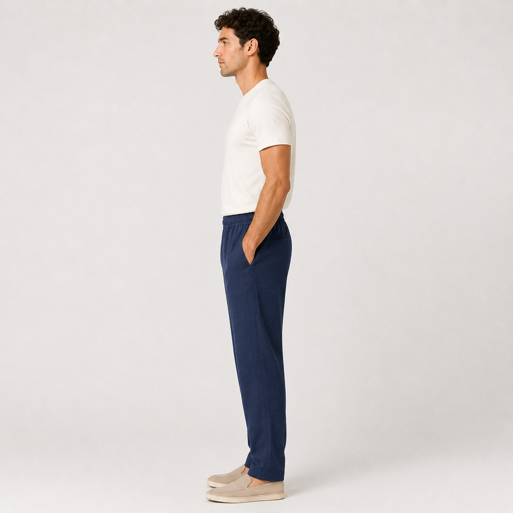 Man wearing a white shirt and navy pants standing against a plain background