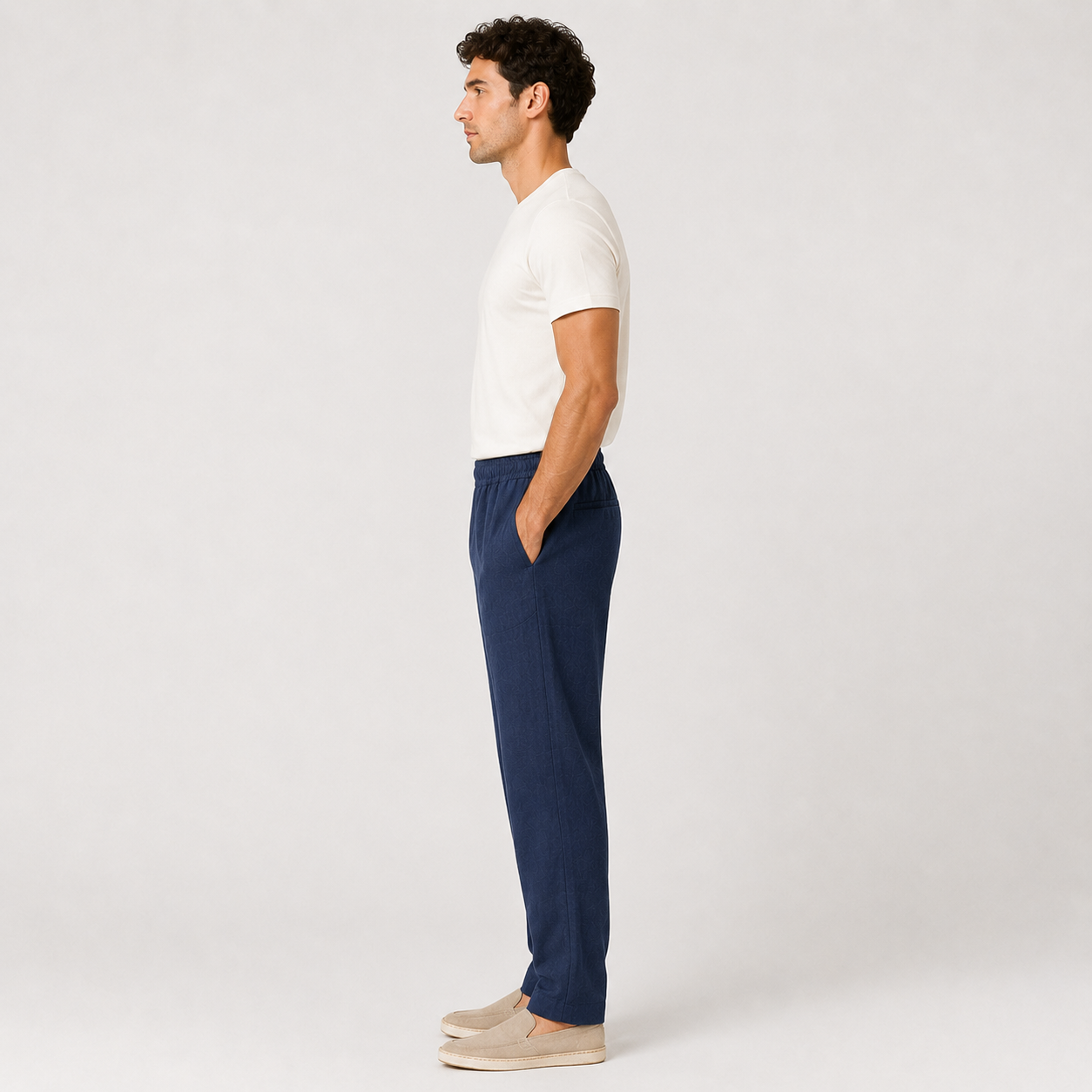 Man wearing a white shirt and navy pants standing against a plain background